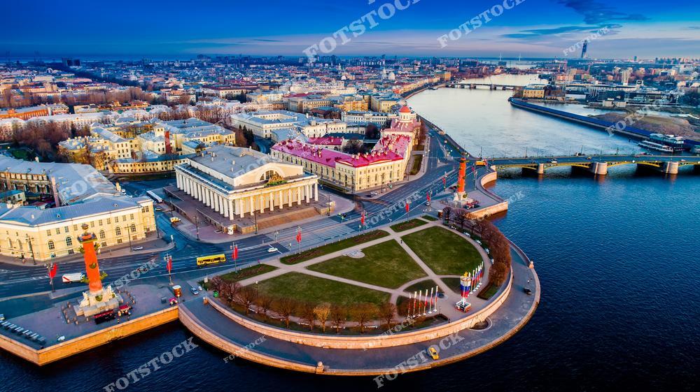 На фотографии изображена Стрелка Васильевского острова с ее знаковыми Ростральными колоннами и величественным зданием Биржи. Мосты и набережные, видимые на заднем плане, подчеркивают уникальный облик Петербурга, соединяющего архитектуру с водными пространствами. Вечернее небо добавляет глубины и романтики городской панораме.